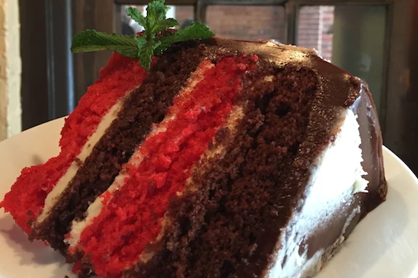 A close-up of a large slice of cake with white, brown, and red layers