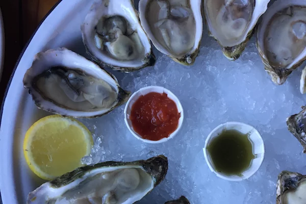 Overhead shot of raw oysters with cocktail sauce, mignonette, and a lemon slice