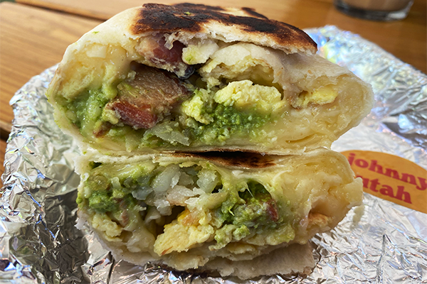 A breakfast burrito sliced in half and stacked one on top of another. The burrito has eggs, bacon, potatoes, and more.