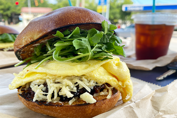 A breakfast sandwich with sausage, eggs, and arugula on a bun
