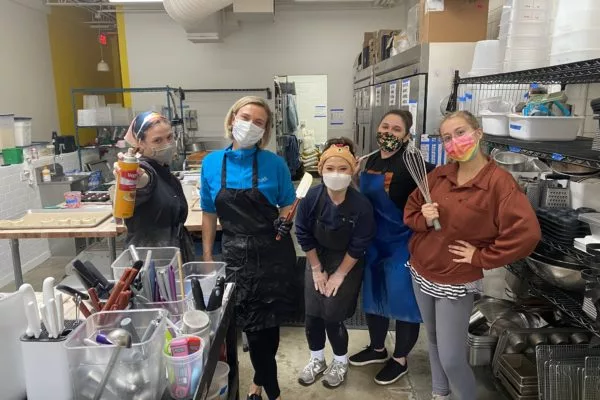 A group of five employees in a kitchen with masks, in various poses