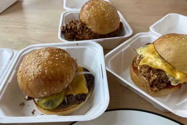 Three sandwiches in white boxes: a cheeseburger, a fried chicken sandwich, and a fried chicken and egg sandwich