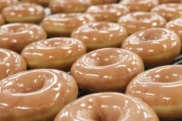 A close-up of several Krispy Kreme donuts, glimmering with a translucent glaze