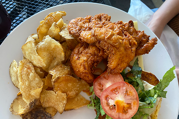 Fried chicken tenders on a bun with tomato and lettuce and a side of chips