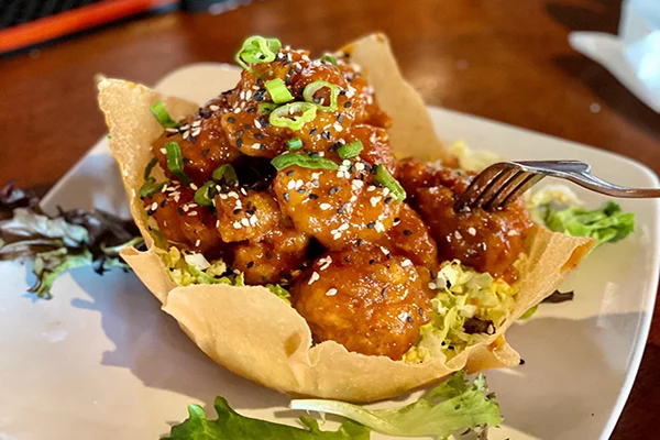 A fried wonton plate full of crispy sauced shrimp topped with sesame seeds and scallions