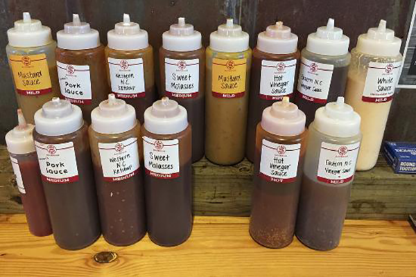 Two rows of bottles of BBQ sauce with various labels and colors