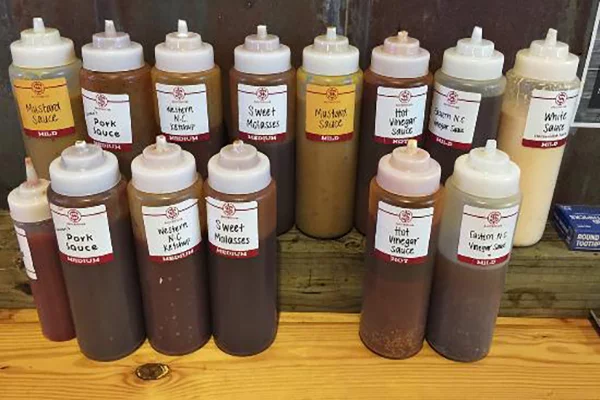 Two rows of bottles of BBQ sauce with various labels and colors