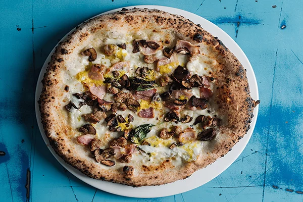 A breakfast pizza on a white plate with a blue background