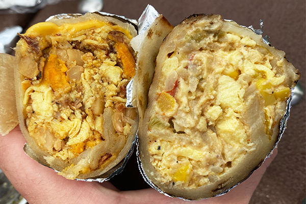 Two densely-packed breakfast burritos cut in half and displayed to the camera in a hand