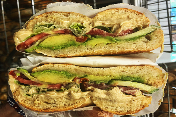 A bagel sandwich topped with avocado, tomatoes, and more