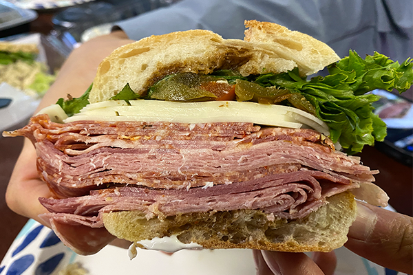 A close-up of a sandwich with multiple Italian meats, cheeses, and other toppings