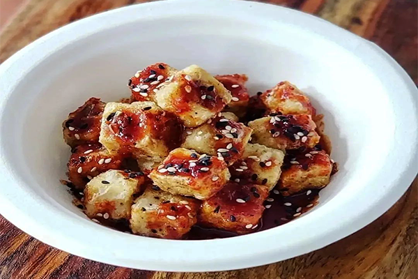 Fried tofu cubes with dark red sauce and sesame seeds