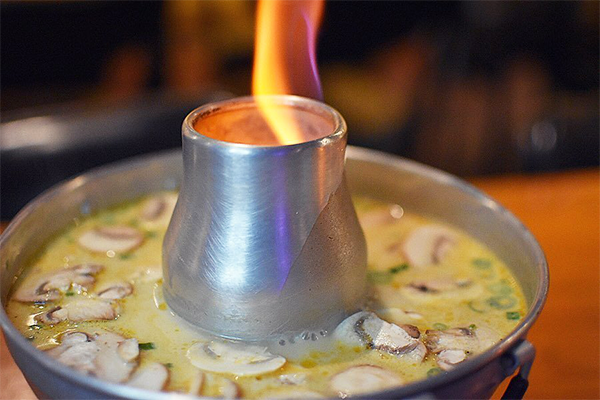 Coconut soup with mushrooms in a silver bowl with a flame in the middle