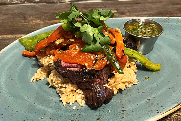 Hanger steak over potatoes with veggies and chimichurri on top