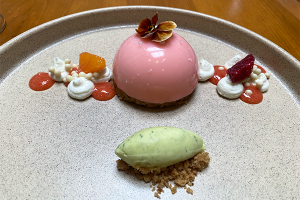 Pink mousse with flower on top and green ice cream underneath it with walnut crumbs