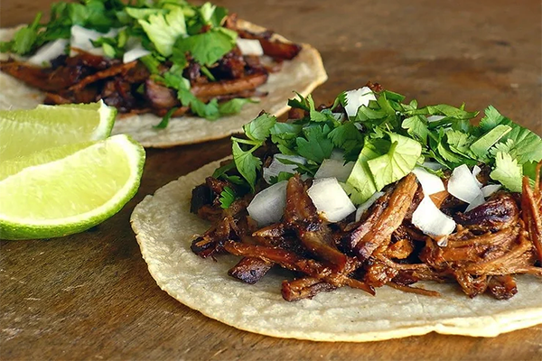 Tacos with carnitas, cilantro, and onion with lime wedges