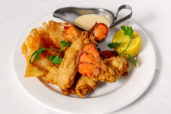 Three fried lobster tails with a lemon, potato chips, green garnish, and a sauce on the side