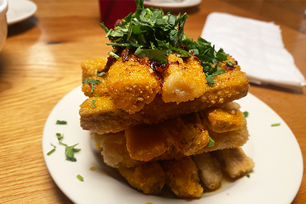 A stack of fried eggplant fries topped with cilantro, chili crisp, and green onions