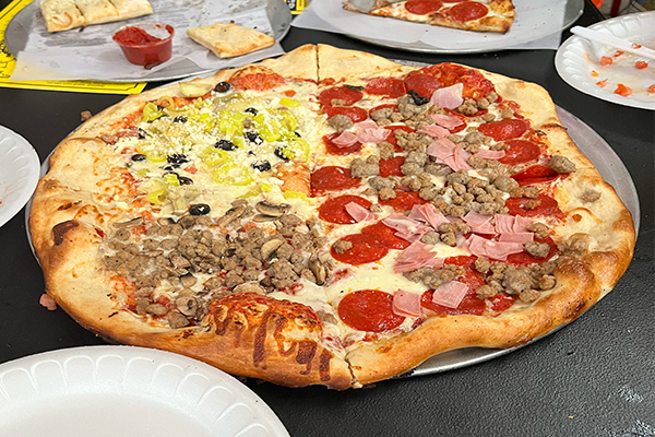 Pizza split into four quadrants: one with banana peppers and olives, meat-lovers, and sausage and mushrooms