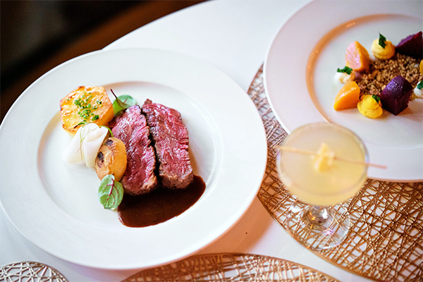 Plate with steak and a plate with a beet salad with a yellow drink in between