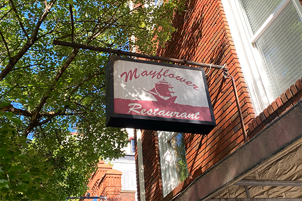 A sign reading "Mayflower Restaurant" with a tree and brick wall in the background