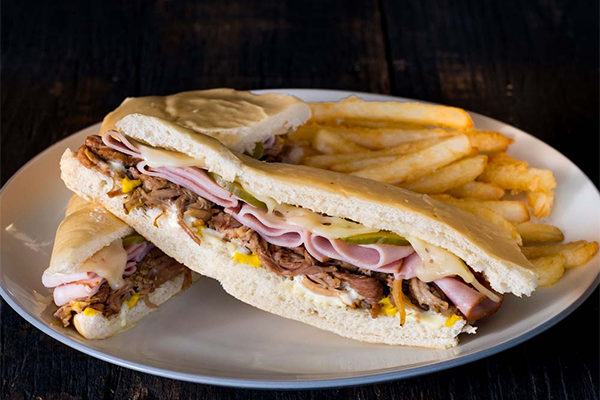 Cuban sandwich with roast pork, ham, cheese, pickles, and mustard with fries in the background