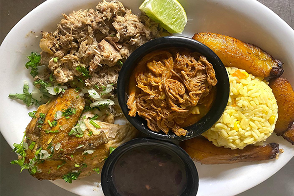 Cuban platter featuring shredded beef, roasted pork, beans, plantains, and green garnish on top