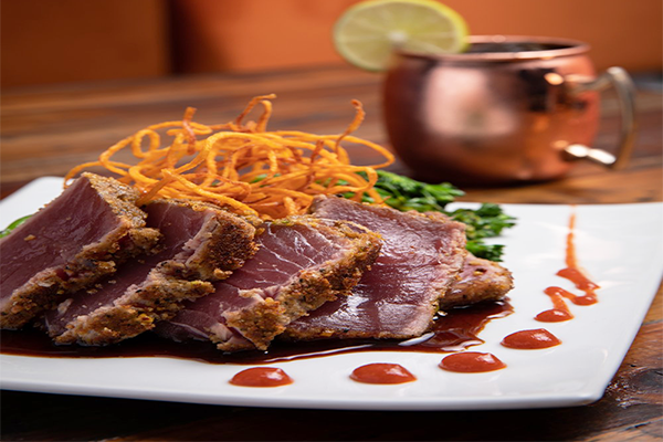 Sliced tuna with onion straws and a copper mug in the background