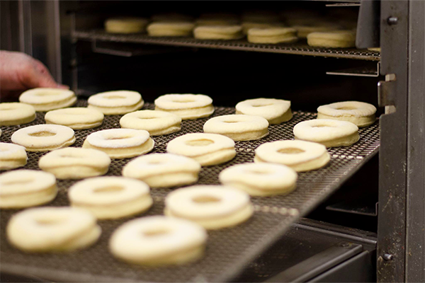 Uncooked donuts on wire rack coming out of an appliance