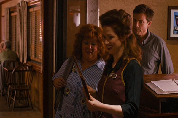 A hostess leading a man and a woman from a host stand with a menu