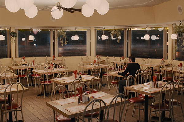 A man sitting alone at a table in a large circular dining room with windows along the curved wall