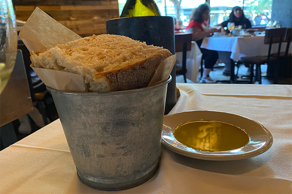 A silver bucket with chunks of artisan bread and a dish of olive oil next to it
