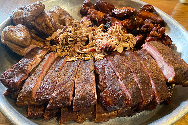 A full silver dish with ribs, pulled pork, smoked chicken, and sauced chicken wings