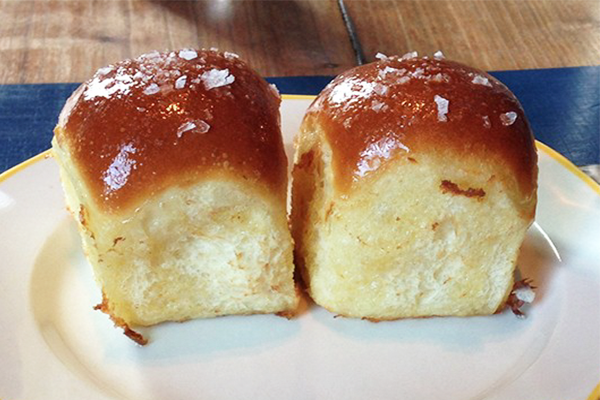 Two dome-shaped house rolls with flaky salt on top on a white plate
