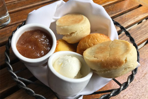 Basket of biscuits and corn muffins with honey butter and a fruit spread