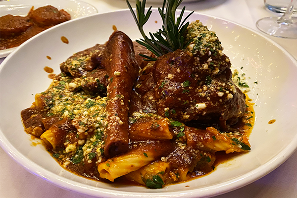 A dish of osso bucco with a chunk of braised meat and a bone with pasta