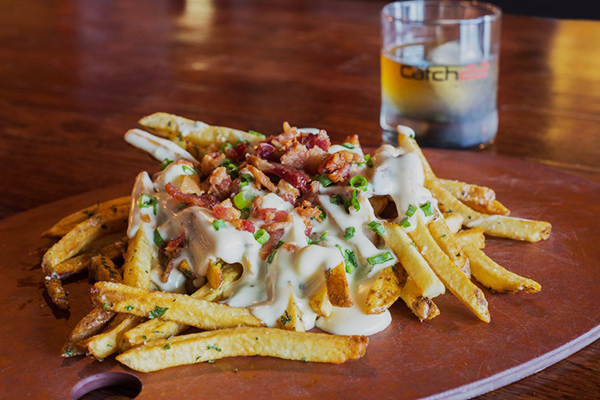French fries on a plate topped with cheese sauce, bacon, and green onions