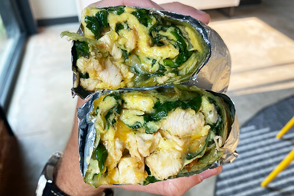 A stacked breakfast burrito wrapped in foil and stuffed with chunks of chicken, scrambled eggs, spinach, and cheese