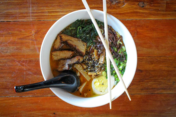 Overhead shot of ramen with pork, eggs, scallions, and more with chopsticks and a spoon