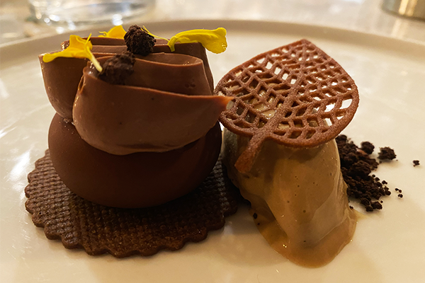 Round chocolate cake topped with a creamy frosting next to a coffee ice cream topped with an edible leaf