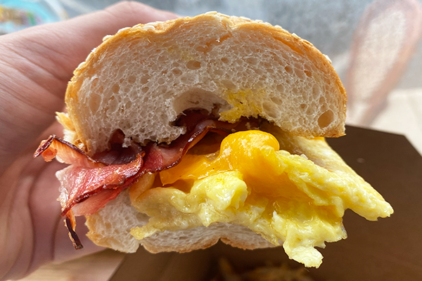 Egg, cheese, and ham sandwich on a sub roll being held in a hand