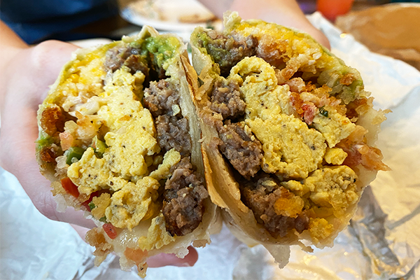 Breakfast burrito cut in half, showing eggs, pico de gallo, sausage, and more