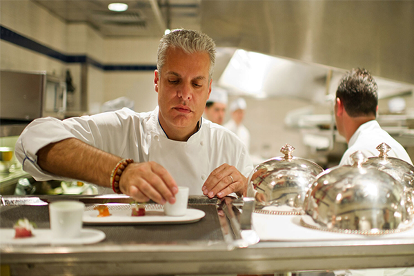 A chef preparing a dish on a white plate with the kitchen in the background