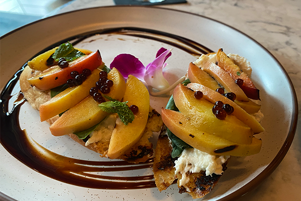 Two pieces of toast with slices of peach and a spread of cheese