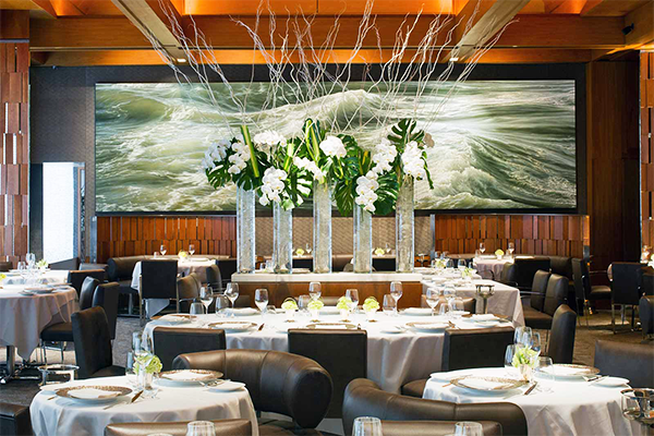 The interior of a restaurant with leather chairs, tablecloth, and a large flower display in the center