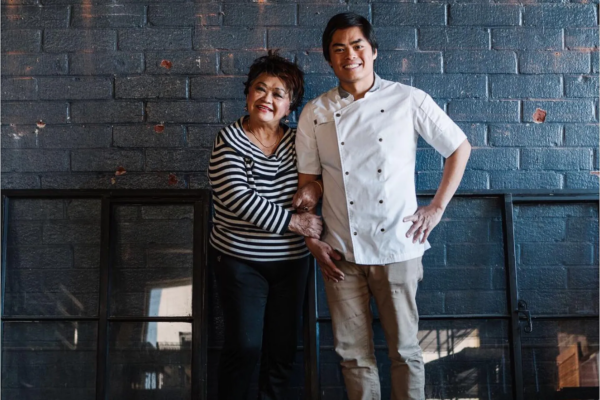 A chef in chef's whites posing with his mother, who is holding his arm