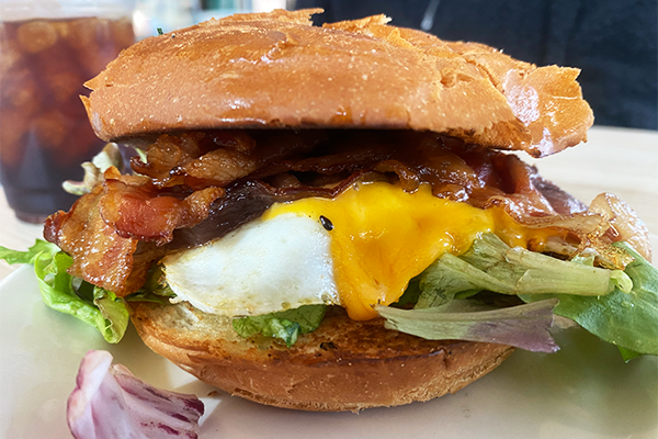 Fried egg, bacon, cheddar cheese, and greens on a soft roll on a white plate