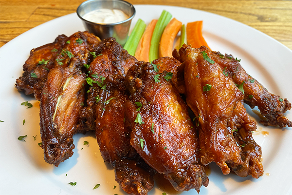 A plate of chicken wings with carrots and celery in the background along with a ramequin of ranch