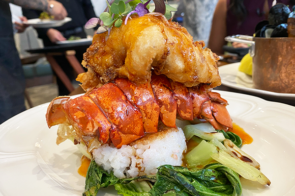 Fried lobster tail on top of a red lobster shell on top of a bed of rice with greens