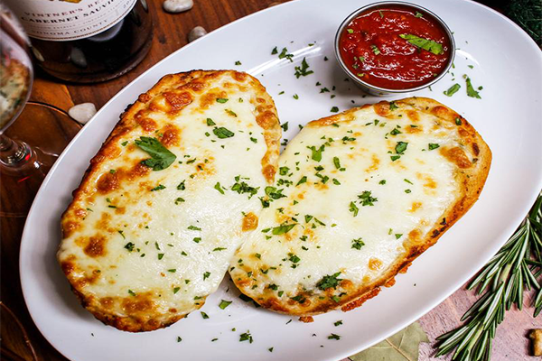 Two slices of cheesy garlic bread topped with green herbs on a white plate with a side of marinara sauce